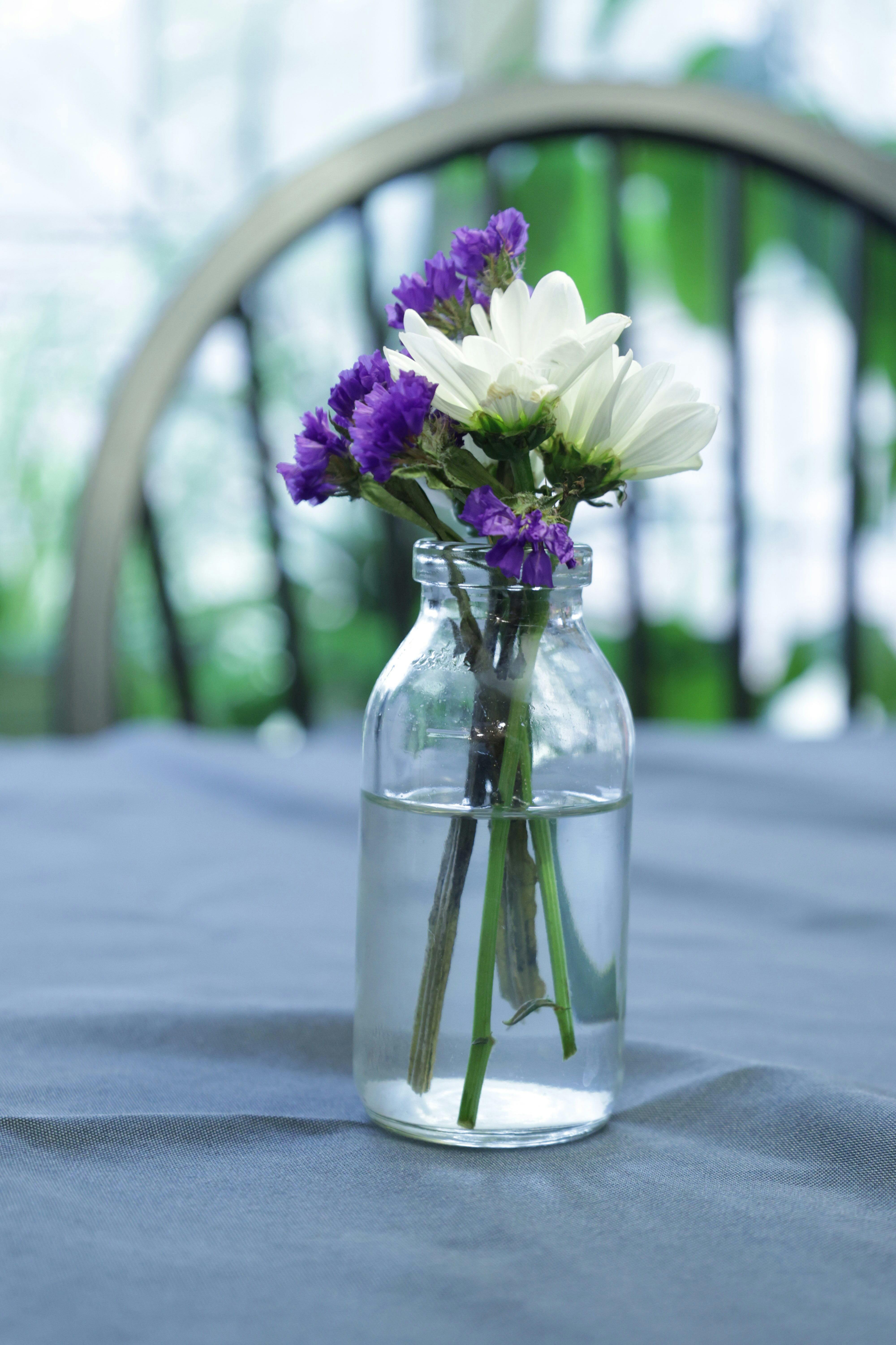 Purple and white flowers in glass bottle on tablecloth